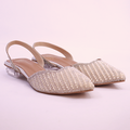 Gold studded flats worn with beige pants on a reflective floor.